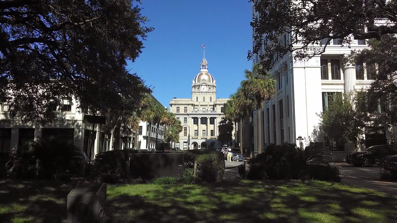Savannah City Hall with its gold dome, viewed along a tree-lined downtown street.