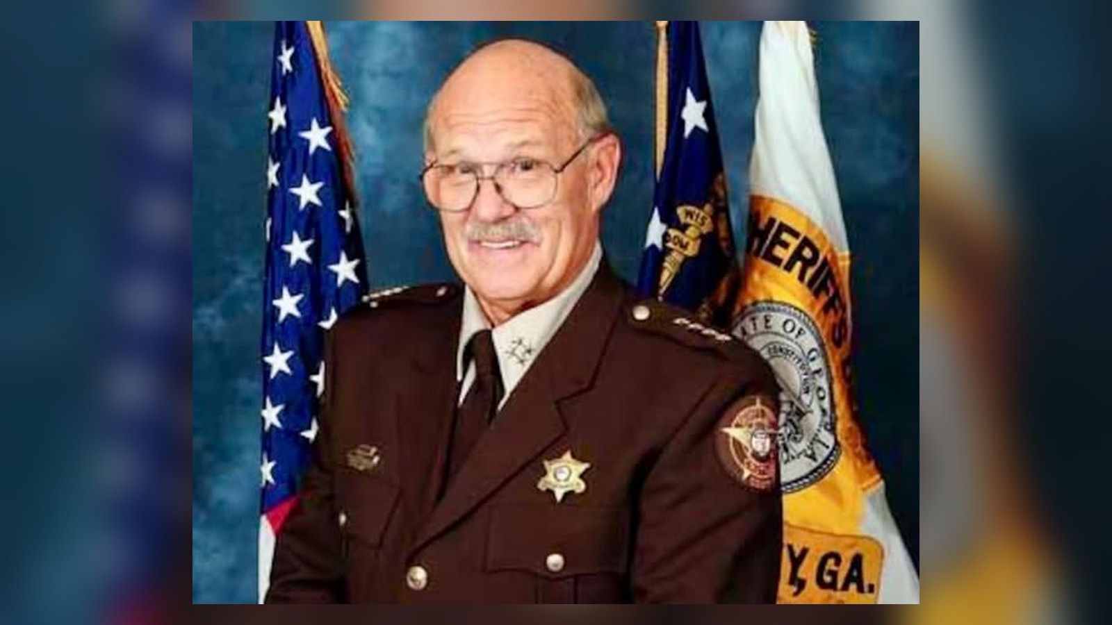 Retired Chatham County Undersheriff Donald Edwin “Donnie” Anderson, Sr., in uniform with U.S. and sheriff’s office flags behind him.